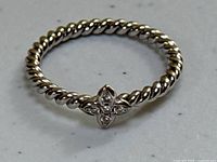 Close-up top view of ring on white background showing twisted rope band and diamond flower motif.