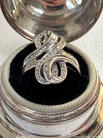 Front view of ring in round box showing swirling bypass design and diamond rows