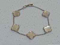 Full view of the bracelet laid flat showing six clover motifs connected by chain and lobster clasp