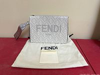 Front view of grey printed leather Fendi Roma clutch displayed on red surface with dust bag and authenticity card visible.