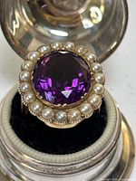 Top view of ring in display case showing faceted amethyst and pearl halo.