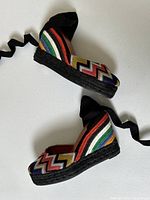 Side view of both shoes on white background showing multi-colored zig zag upper and black jute wedge sole.