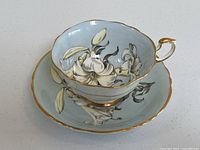 Angled front view of teacup seated on saucer showing floral pattern and gold trim