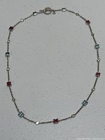 Full view of the necklace laid flat showing alternating square gemstones and diamonds.