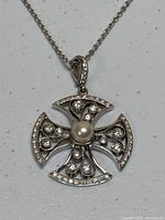 Close-up of platinum cross pendant front showing diamond settings and central pearl