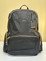 Front view of backpack showing main compartment, front zippered pocket, blank leather tag holder attached
