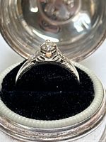 Front view of ring in round silver-tone box