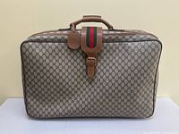 Front view of suitcase showing GG canvas pattern, leather trim, Web stripe and buckle