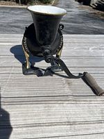 Side view of the antique Spong No. 4 coffee grinder showing the hand crank, black metal body with gold accents, and funnel-shaped white hopper.