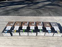 Seven new/open box Baldwin door knobs and deadbolts lined up on wooden surface. Boxes labeled with product images and details.