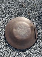 Copper gong lying on gravel showing front side and attached hanging cord.