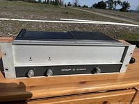 Front view of the Crown D150A amplifier showing the silver front panel with three knobs and two indicator lights labeled 'IOC'. The model and brand are visible.