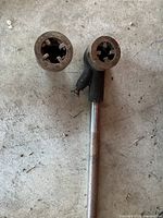 Pipe threader showing the T-handle and threaded dies with rusty and worn metal surfaces.