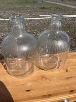 Two large clear Pyrex glass bottles on wooden surface outdoors.
