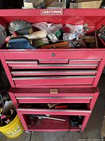 Top view of open red Craftsman toolbox showing saw blades, sanding sponge, screwdrivers, and various hand tools inside.