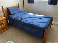 View of assembled single wooden bed with blue bedding, nightstand visible beside it