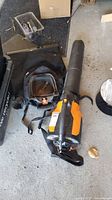 Full view of Worx leaf blower with shoulder strap and attached collection bag on floor.