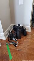 Three binoculars and two film cameras arranged on the floor corner