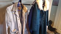 Two winter coats hanging on hangers including a ladies black wool coat with a faux fur collar and a men's beige jacket.