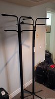 Photo of two black metal coat racks standing side by side against a wall, showing multiple horizontal arms for hanging and a four-legged base.