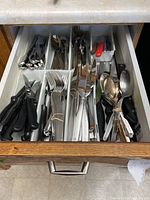Top view of an open drawer showing organized cutlery including forks, knives, spoons, and some kitchen gadgets in a white plastic drawer organizer