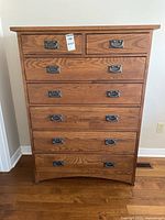 Front view showing seven drawers, wood grain finish, metal drop handles, label on upper drawer