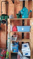 Photo of wooden shelves with a blue watering can, small red and white containers, clear bottles, and a large blue storage bin. Wooden wall background.
