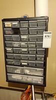 Full view of black wall-mounted hardware organizer with multiple clear plastic drawers containing assorted hardware.
