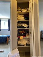 Closet with multiple shelves filled with folded linens and towels stacked in piles.
