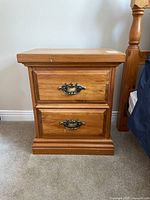 Front view of wooden nightstand showing two drawers with brass handles and condition of finish.