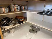 Wide view of shelves holding various pots, frying pans, pot lids, and a silicone baking tray.