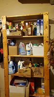 Front view of the pine shelving unit showing four shelves with various household items stored on it (not included in the lot).