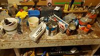 Worn wooden workbench surface cluttered with paint cans, hand tools like screwdrivers and wrenches, small metal hardware pieces, and containers