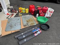 Full set of items arranged on ground outside, showing gasoline cans, oil pans, garage rugs, and assorted containers