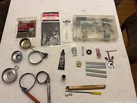 Overview photo showing multiple car tools and parts arranged on a table, including oil filter wrenches, clamps, small hardware items, tubes of adhesive, and a hammer.