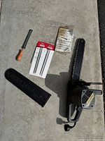 Full lot layout showing McCulloch Electramac electric chainsaw with attached chain and bar, plastic bar cover, sharpening files in packaging, user manual in plastic, and wooden-handled sharpening file tool.