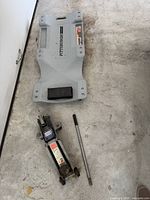 Top view of Pittsburgh creeper and hydraulic floor jack with detached handle on a concrete floor.