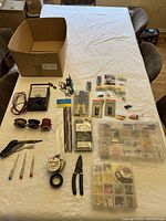 Overview of electrical tools and supplies on table showing multimeter, soldering iron, wires, tape, terminals, cutters, testers, and organizer boxes