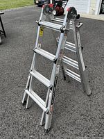 Photo showing ladder set in A-frame configuration on asphalt surface, capturing the structure and locking hinges.