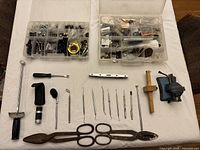 Top view of lot showing tools such as picks, magnifiers, torque wrench, marking gauge, bench vice, and long metal tool along with plastic hardware organizer boxes.