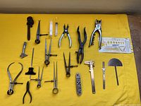 Full view of the varied odd tools arranged on a yellow cloth including calipers, dividers, pliers, syringes, wrench, scraper, and measuring devices.