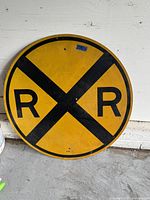 Front view of the circular railroad crossing sign showing yellow background with black 'X' and 'R R' letters.