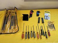 Wide view of all tools laid out on yellow surface including screwdrivers, hex keys, drill bits, Mr. Grip pack, and files pouch