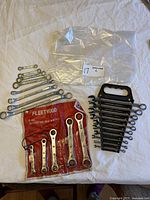 Overall lot of used wrenches on white cloth including loose combination wrenches, wrenches on a black plastic holder, and the red Fleetwood pouch with ratcheting box wrenches.