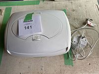 White plastic Prince Lionheart electric baby wipe warmer with lid closed. Power cord attached with plug visible.