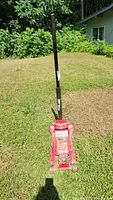 Full view of the red Torin Black Jack hydraulic car jack on grass, showing long black handle and lifting base.