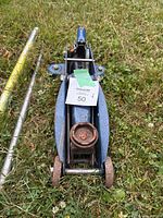 Top view of blue car jack showing rust on lifting pad and wheels on grass.