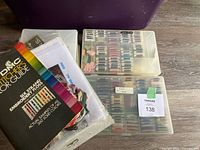 Embroidery floss skeins in two compartmentalized plastic cases with color guide and cross stitch patterns.