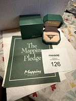 Ring and packaging overview: green Mappins outer box, ring box, branded booklet, and MaxSold lot number tag