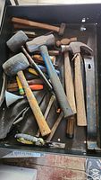 Top-down view of drawer containing various hammers and mallets of different sizes and types, mostly well-used with some paint marks and rust.